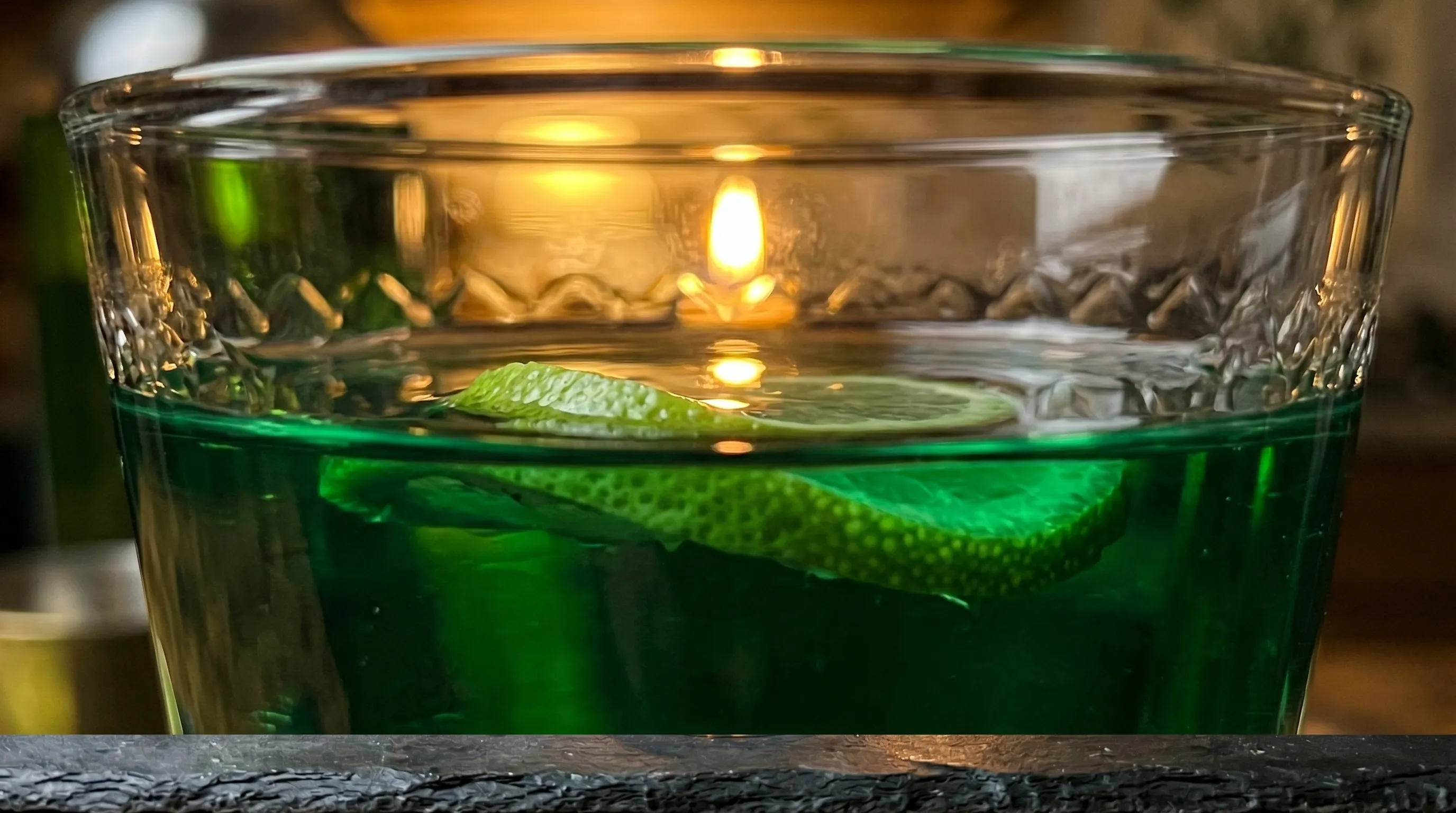 Eye-level with the emerald meniscus, a single candle flame reflected on the surface